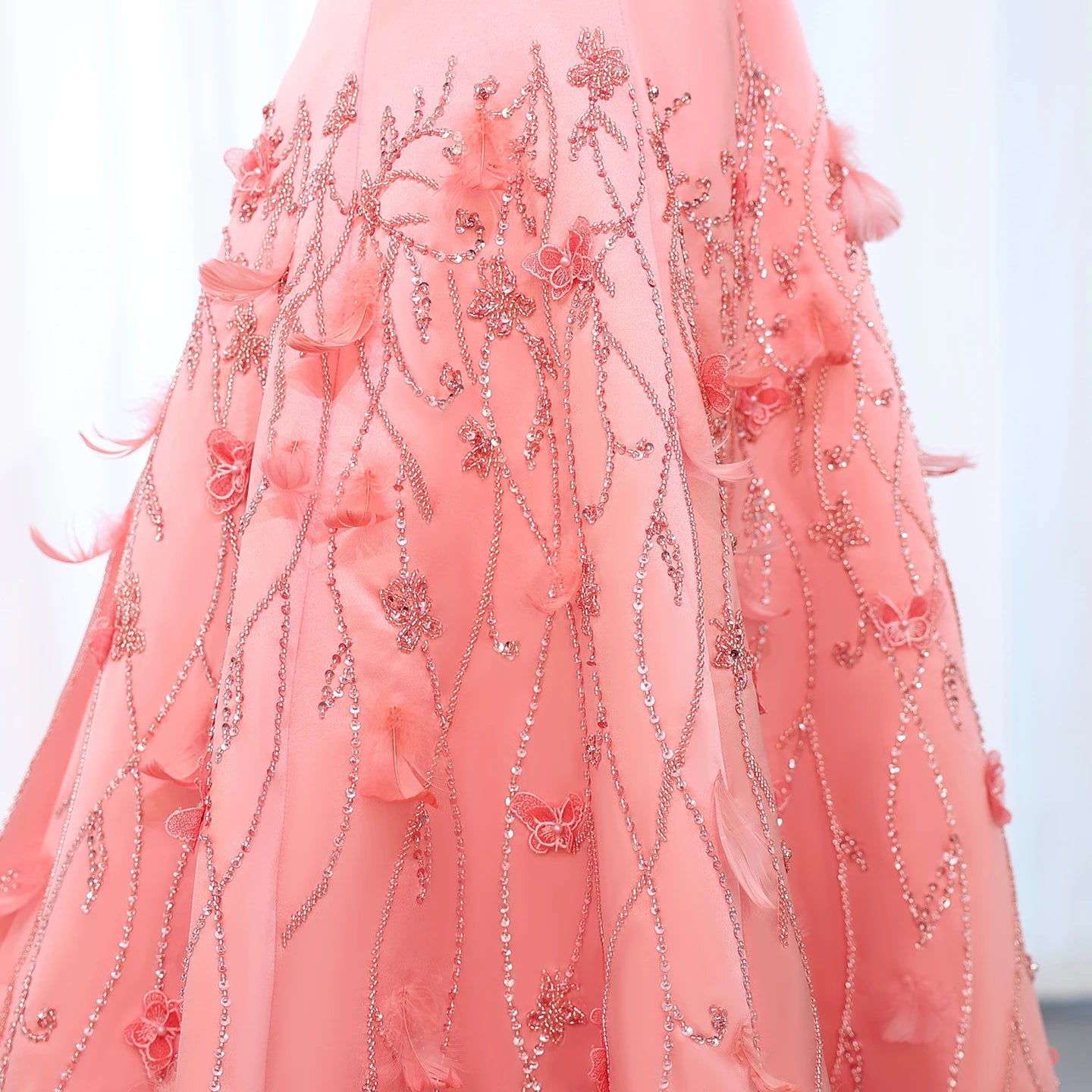 Close-up of a pink ballgown dress with sparkly intricate floral and butterfly embellishments on a white background