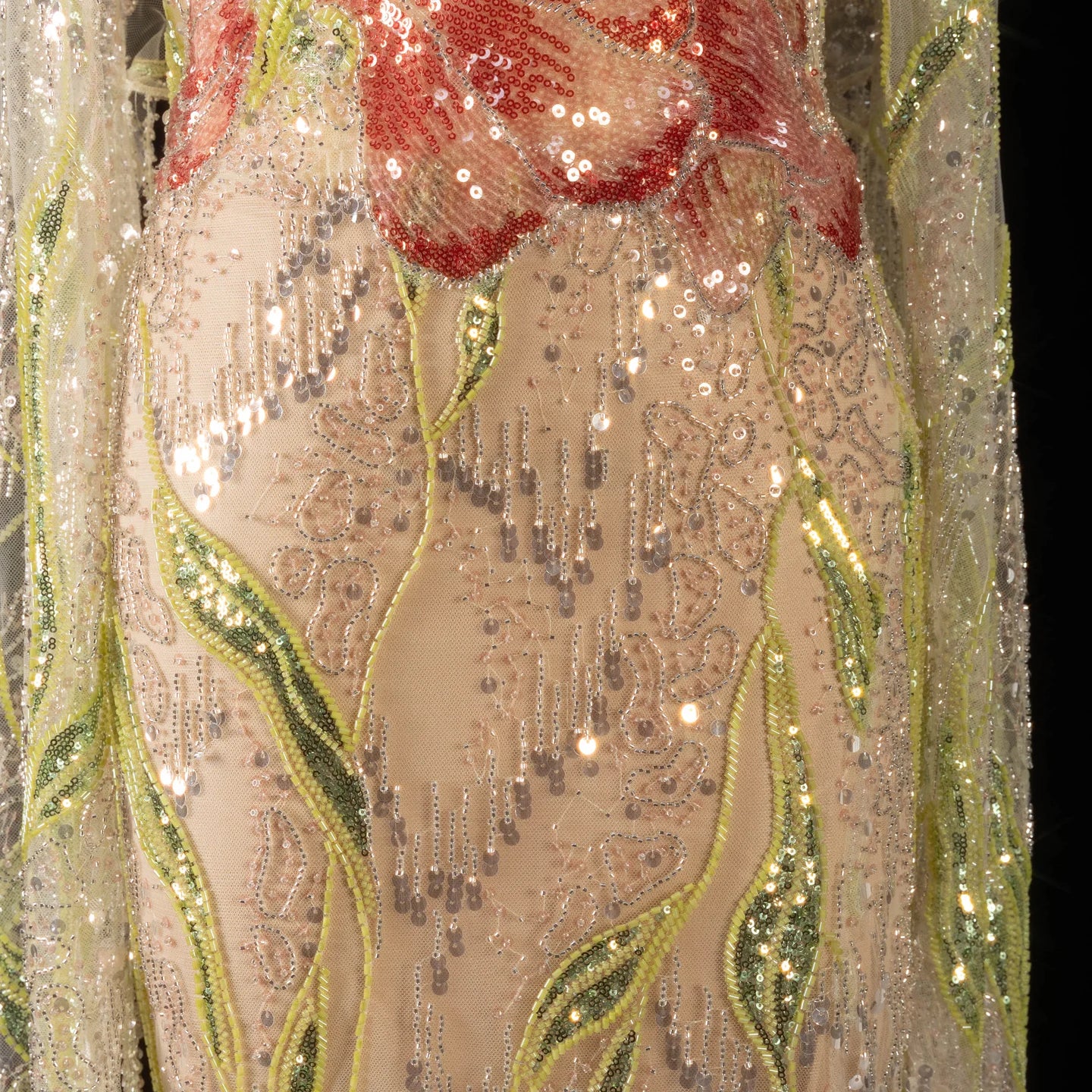 Decorative fabric close up of a luxury evening gown dress with red floral and intricate shinmering embellishment patterns on a black background