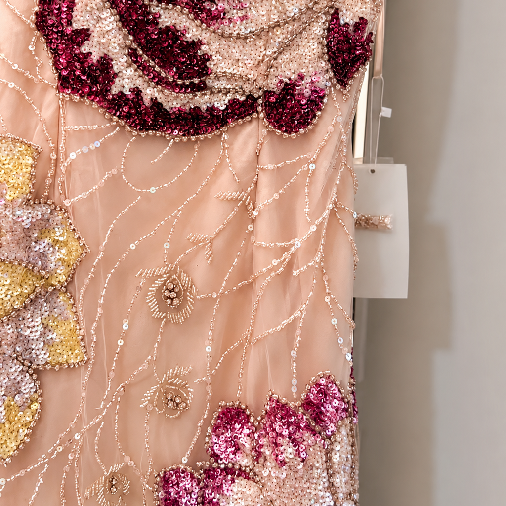 Close-up of a pink dress with intricate beadwork and floral patterns.