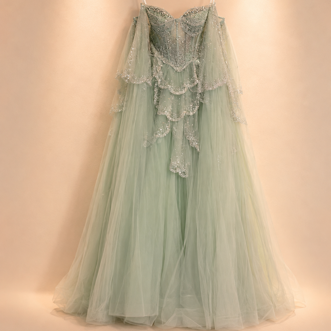 Luxury fashion sage Green evening ballgown with shimmering fantasy like details on a wooden hanger against a beige background