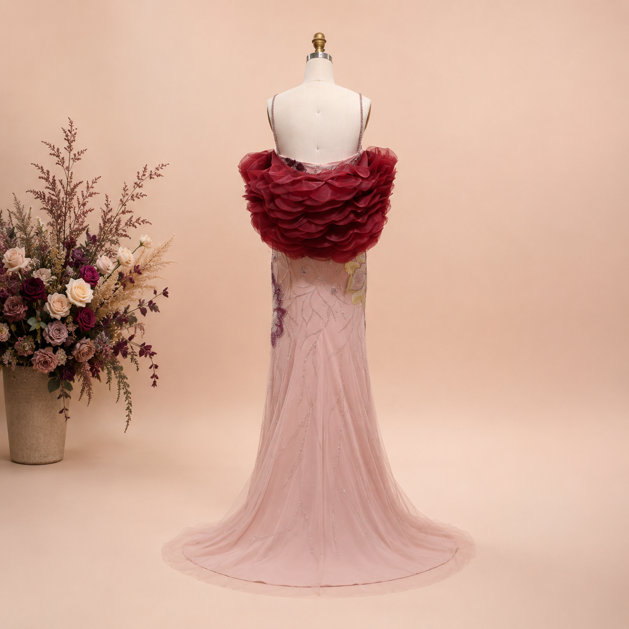 Mannequin wearing a long elegant pink gown with shiny crystal beaded details with a bouquet of flowers on a beige background