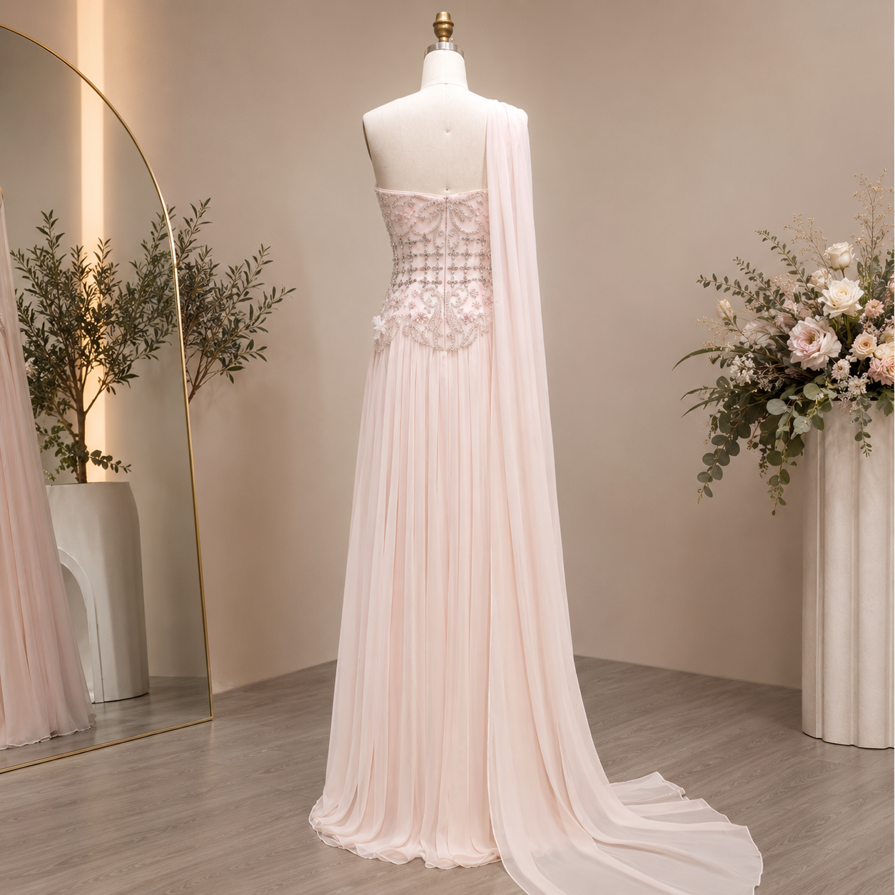 Elegant blush pink long evening gown on a mannequin with stunning bead work and floral decorations and a mirror in the background.