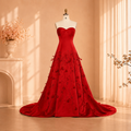 A stunning red strapless luxury ball gown with a sweetheart neckline and 3D floral embroidery, with beautiful beadwork details, displayed on a dress form mannequin in a warm, sunlit room with a cream-colored fireplace and curtains.