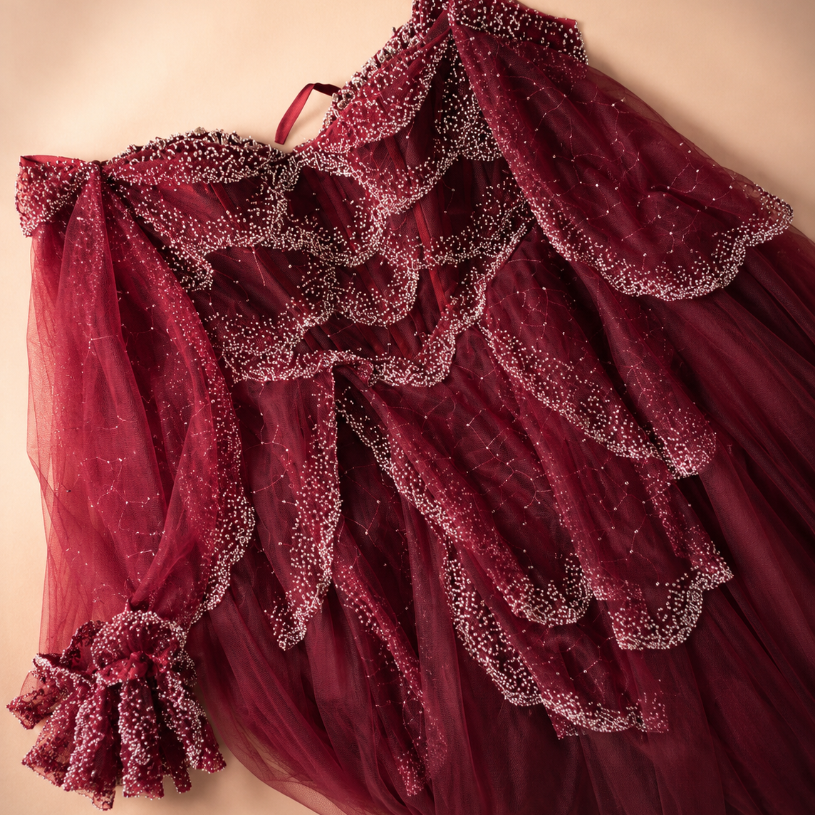 Red evening gown with luxurious shiny beaded details on a beige background
