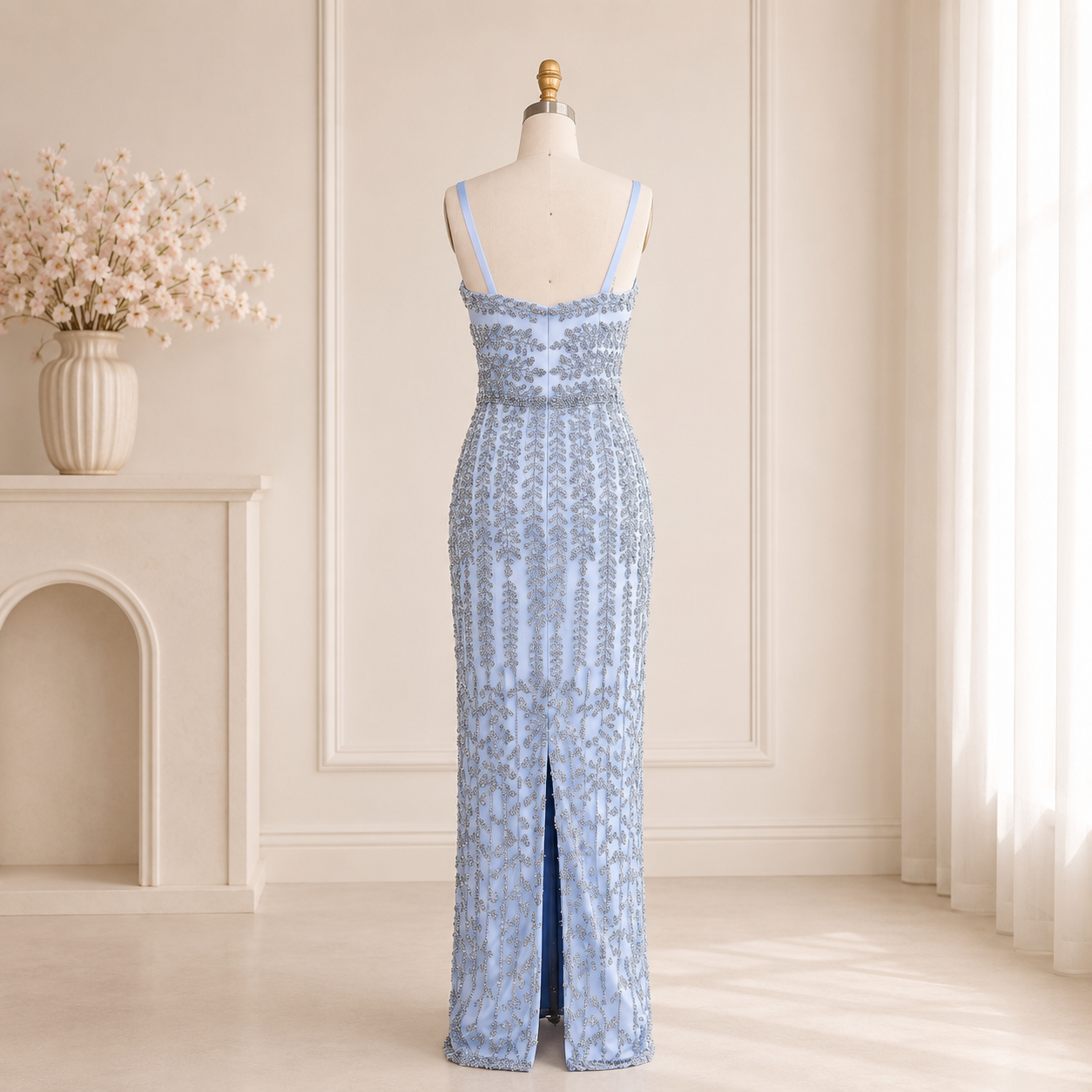 A shimmering silver beaded light blue  sleeveless luxury evening gown dress displayed on a mannequin in a softly lit cream-colored room with a fireplace and sheer curtains.
