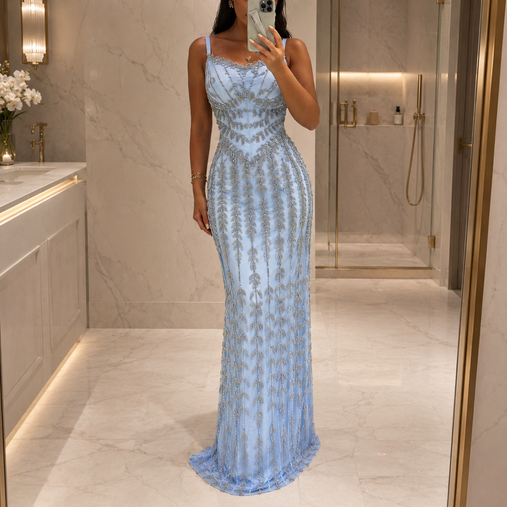 A stunning woman takes a mirror selfie in a bathroom wearing a light blue sleeveless luxury evening gown with detailed shiny silver beaded patterns and a sweetheart neckline.