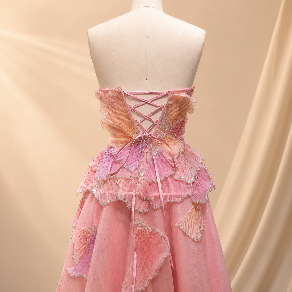 Pink princess luxury ballgown from behind worn on a mannequin,  showing the lace up back and shimmering three dimensional appliqués.