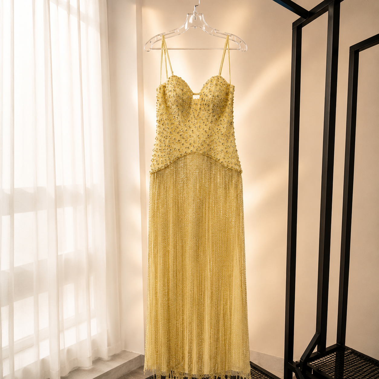Gorgeous shimmering Yellow beaded luxury dress hanging on a rack in a well-lit room with curtains.