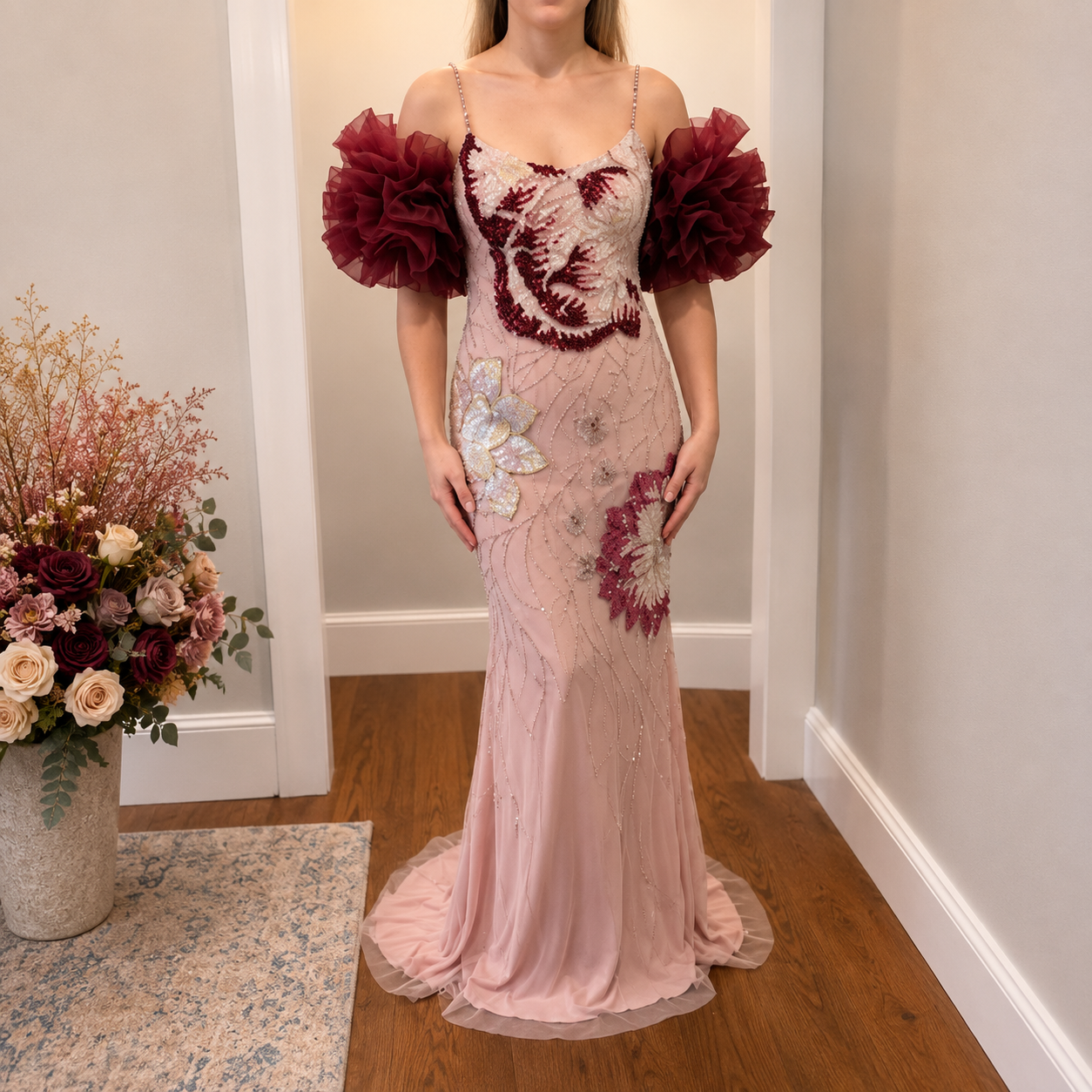 Woman wearing a stunning luxury fashion beaded pink sparkling dress with red shrug accessory in a room with flowers and a rug.