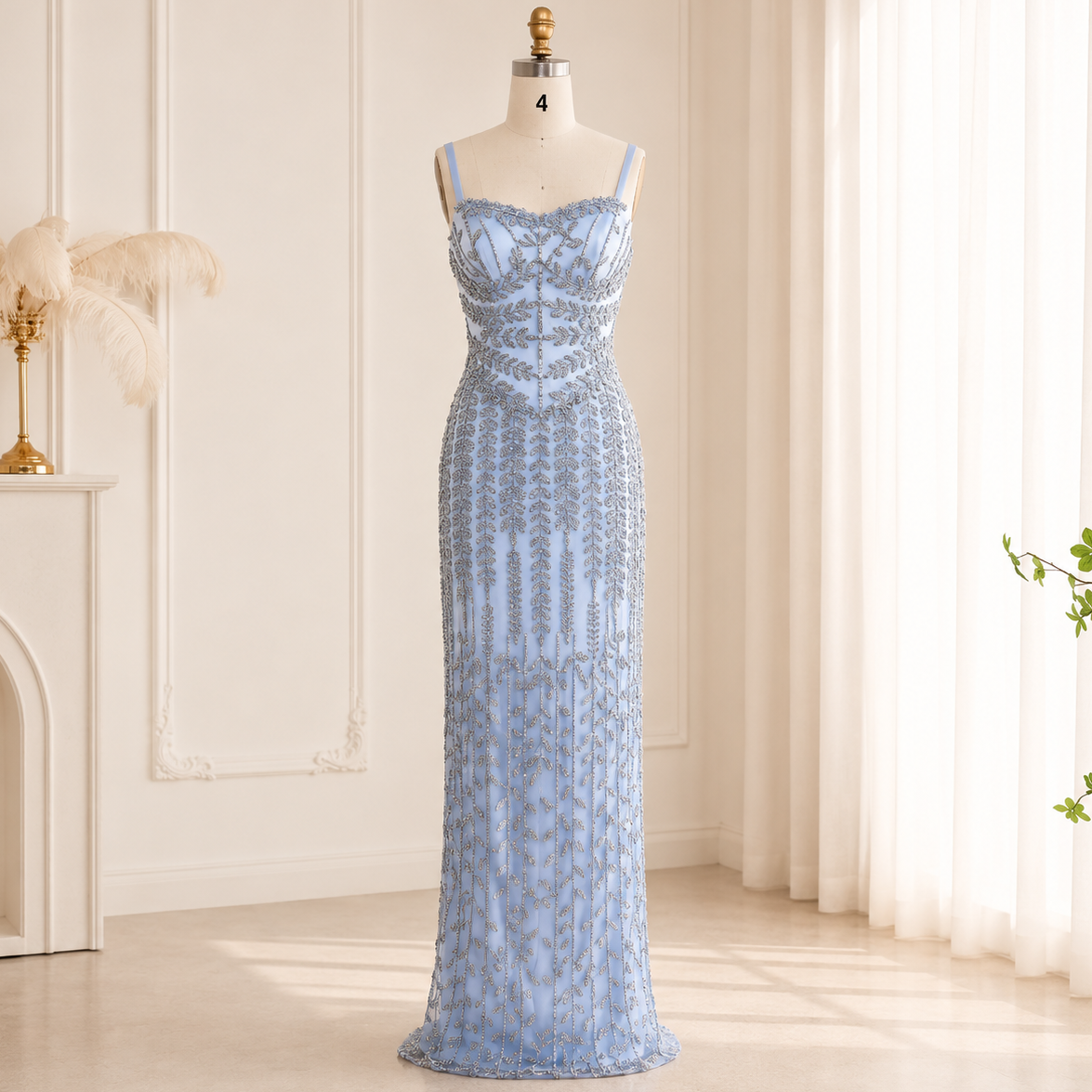 A beautiful light blue beaded floor-length gorgeous evening gown displayed on a mannequin in a bright, elegant room with cream walls, sheer curtains, and a fireplace.
