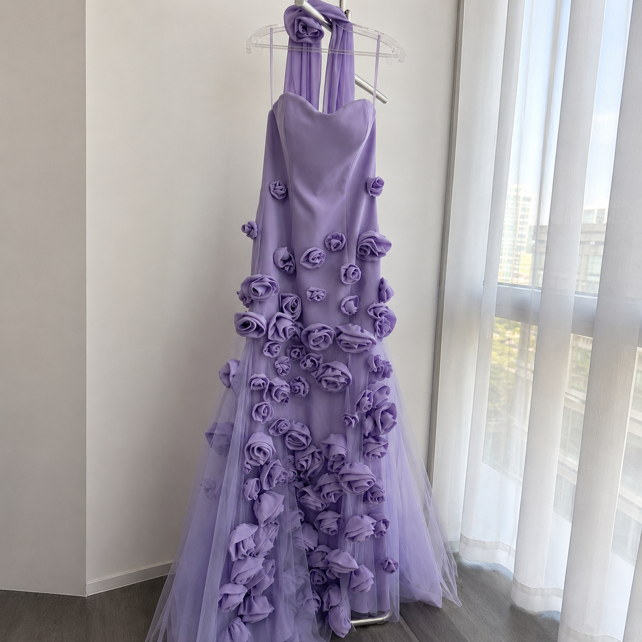Stunning couture fashion luxury Purple prom dress with purple floral details on a hanger in a room with a window.